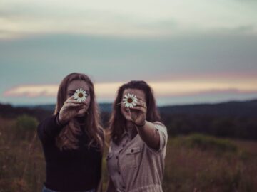 To piger står ude i naturen og holder en blomst i deres hænder.