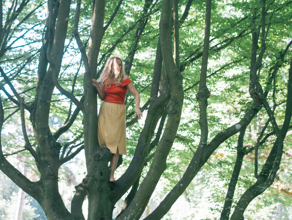 Laura Mikkelsen klatrer i træer iført rød bluse og gul nederdel. 