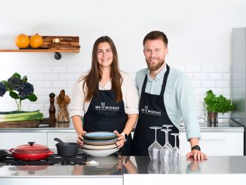 To smilende personer står med forklæder på i et køkken