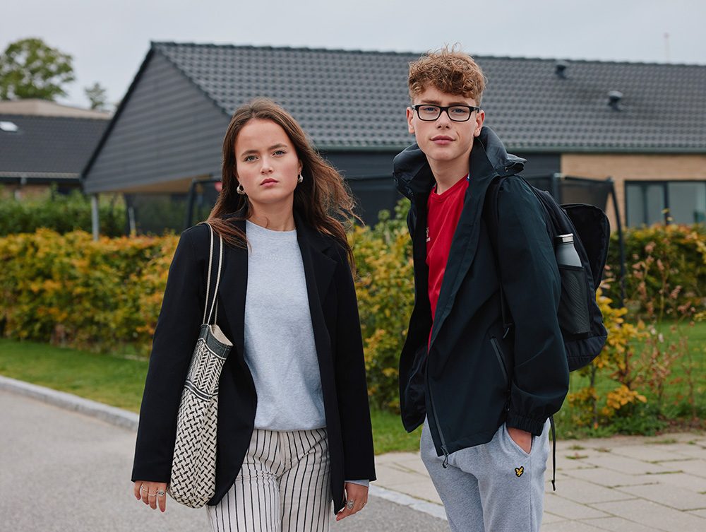 Natasja og William står på vejen foran deres hus med jakke og skoletaske på.