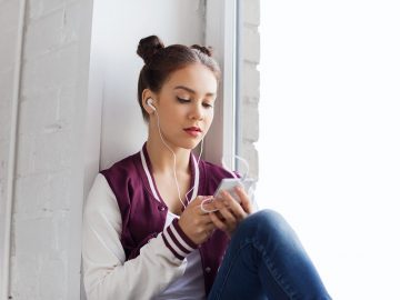 Teenager sidder i vindueskarm og lytter til podcast på sin telefon