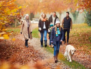 En familie med bedsteforældre, forældre og to børn går gennem en skov med en hund i snor