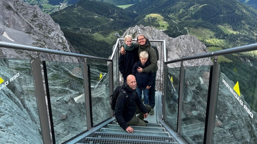 Betina, manden Morten og deres børn står på en trappe omgivet af bjerge.