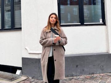 Malou står på gaden iført vintertøj med en kop kaffe i hånden.