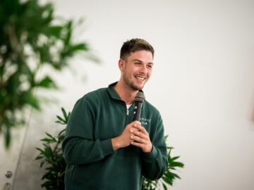 Komiker Oliver Stanescu står på scenen med en mikrofon