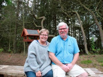 Steen Hansen og konen, Helle, sidder på en bænk i naturen.