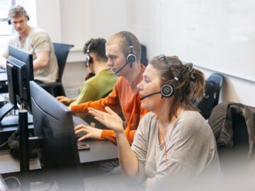 Kvinder sidder og taler i headset foran en computerskærm