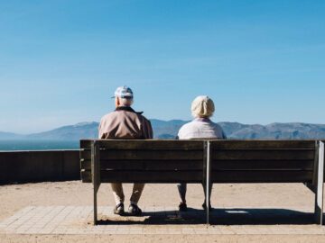 To ældre mennesker sidder på en bæk og ser udover bjerge i horisonten.