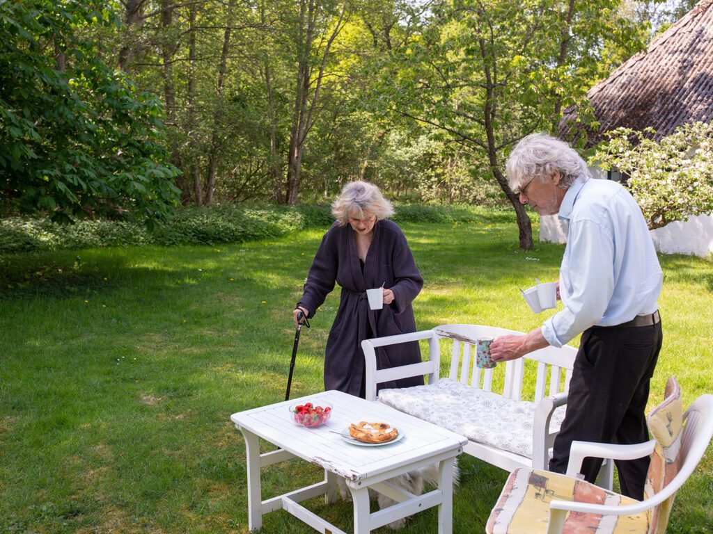 Ulla og manden, Anders, står ude i sommerhusets have og dækker bord.