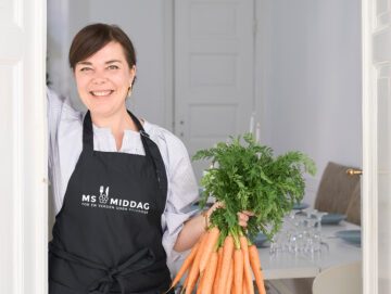 TV-kok og kogebogsforfatter, Louisa Lorang står med et bundt gulerødder i hånden iført et MS middag-foklæde.