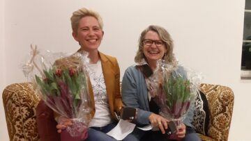 To kvinder der sidder i en sofa og smiler med blomster i hænderne