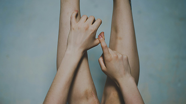 Nærbillede af ben og hænder. Fingrene rører forsigtigt ved hinanden for at symbolisere føleforstyrrelser som symptom på sclerose.