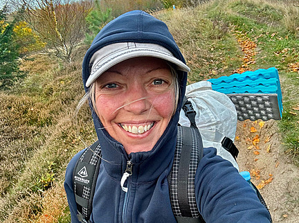 Gitte Holtze har kasket og hættetrøje på samt rygsæk på ryggen. Hun smiler stort.