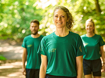 En mand og to kvinder i en skov iført YOU GO T-shirts