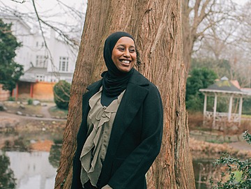 Ibtisam Said står i naturen foran et træ og smiler stort.