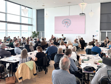 Forskningsformidler i Scleroseforeningen Sidsel Brandt Hasberg interviewer Derya Tireli foran deltagerne ved Forskningsspejlet 2026.